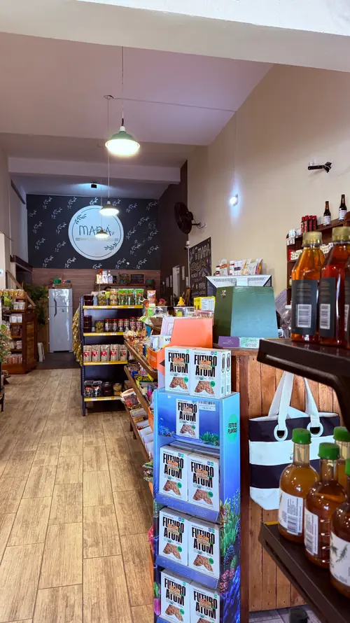 Corredor da loja com piso de madeira, prateleiras de produtos e o logo do Maná na parede do fundo